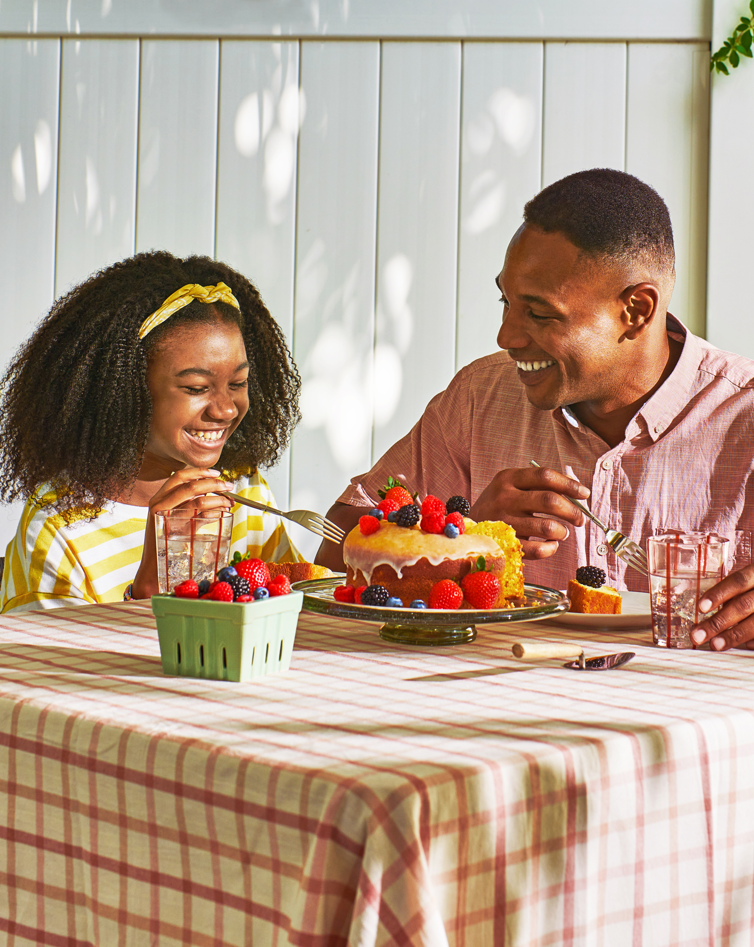 Image of a man and girl at a table smiling with a mixed pound cake with fresh strawberries, raspberries, blueberries, and blackberries.