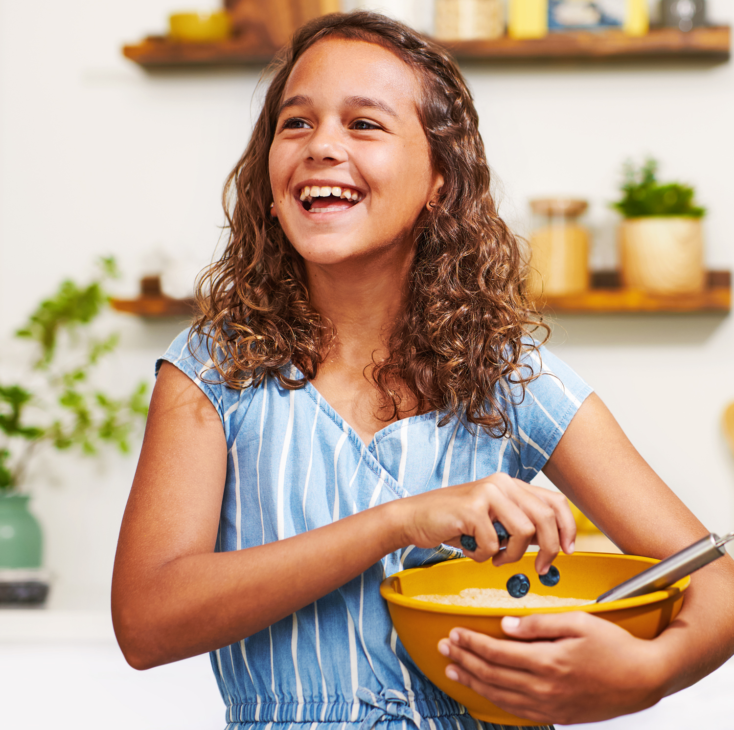 Image of girl smiling while dropping blueberries into a baking bowl